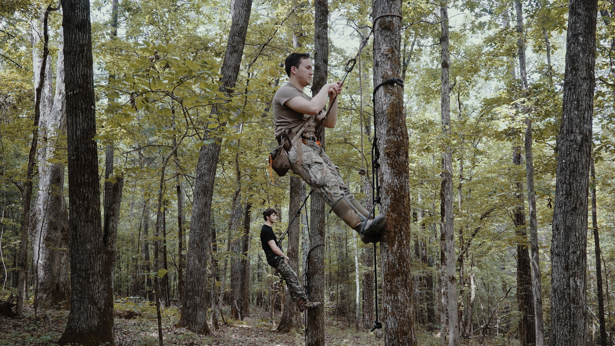 Two men are using the Bandit Climber from Raccoon Rigs in the woods.