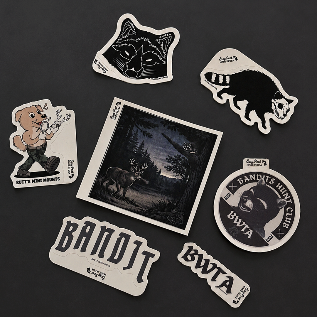 A set of die-cut stickers featuring bandit-themed illustrations and text, arranged on a dark gray background. The stickers include a wolf head, a black-and-white animal silhouette, a cartoon dog holding a bow, a square forest scene with a deer, a round sticker with a bear head and the text 'Bandit's Hunting Club BWTA', and two horizontal stickers reading 'Bandit' and 'BWTA'.