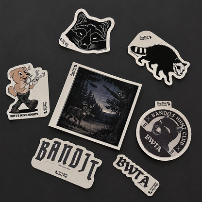 A set of die-cut stickers featuring bandit-themed illustrations and text, arranged on a dark gray background. The stickers include a wolf head, a black-and-white animal silhouette, a cartoon dog holding a bow, a square forest scene with a deer, a round sticker with a bear head and the text 'Bandit's Hunting Club BWTA', and two horizontal stickers reading 'Bandit' and 'BWTA'.